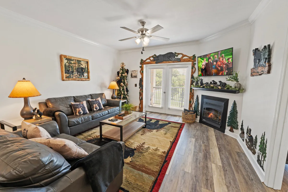 A warm, inviting living room featuring a comfortable sofa, a stone electric fireplace with a flickering glow, a flat-screen TV mounted above, and soft lighting from table lamps. A cozy rug and tasteful décor complete the welcoming atmosphere.