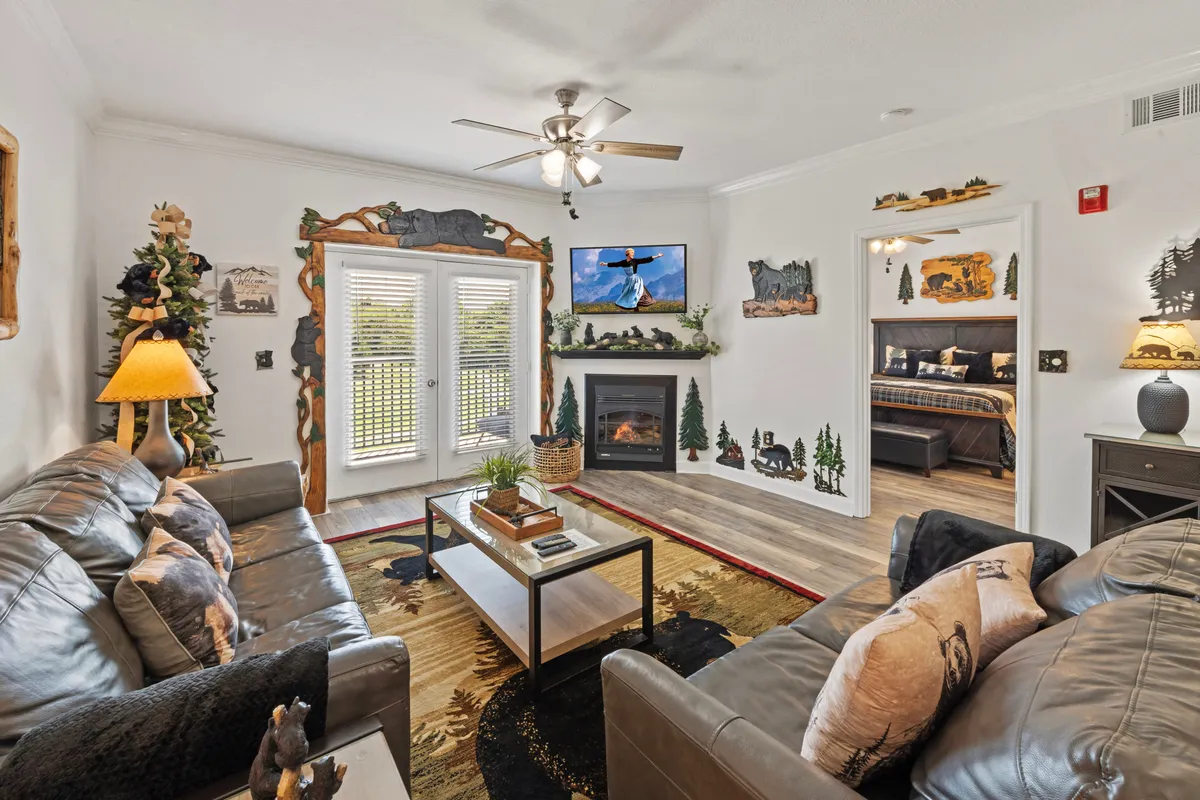 A spacious living area featuring plush leather sofas, a coffee table, a cozy fireplace, wall decor, and a large television. Abundant natural light spills in through the windows, creating a warm, inviting atmosphere perfect for relaxation or spending time with family.