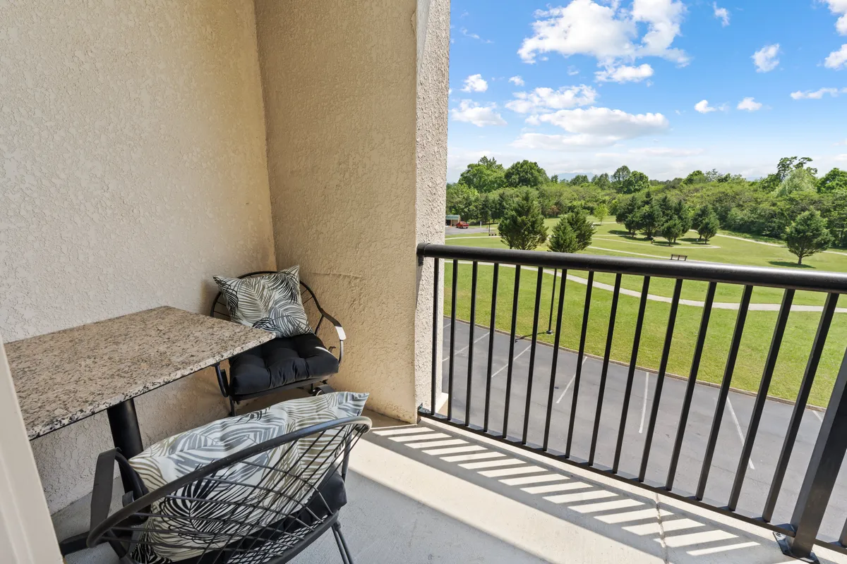 A cozy outdoor patio featuring a small granite-top table and a comfortable wire chair with a cushion, overlooking a lush green lawn and mature trees. The setting feels intimate and is perfect for sipping morning coffee or enjoying a quiet evening as the sun sets over the Smoky Mountains.