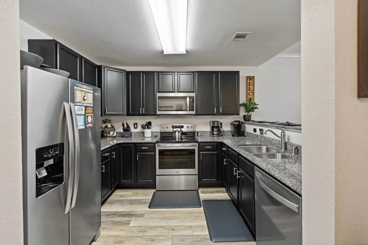 A modern, fully equipped kitchen with stainless steel appliances, dark cabinetry, granite countertops, and a central island—ideal for preparing meals and gathering with family or friends. The kitchen feels bright and inviting, ready for culinary creativity.