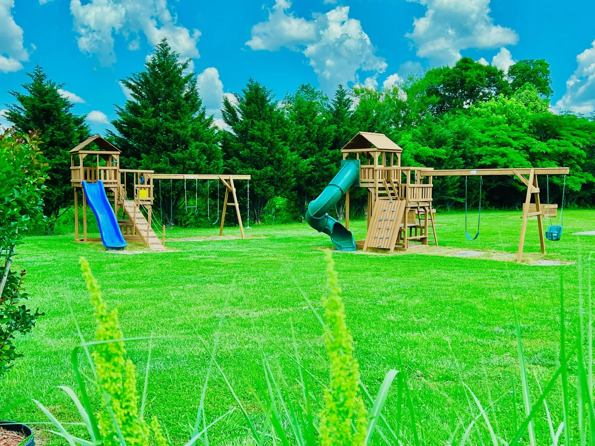 A colorful playground set on lush green grass, complete with swings, slides, and climbing structures. The mood is joyful, capturing children playing and families enjoying time outdoors.