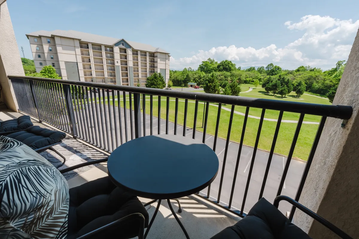 A tranquil balcony setup with comfortable seating and a black table, overlooking green landscape and residential buildings. The area is ideal for relaxing with a partner, enjoying coffee, or unwinding after a day of adventure.
