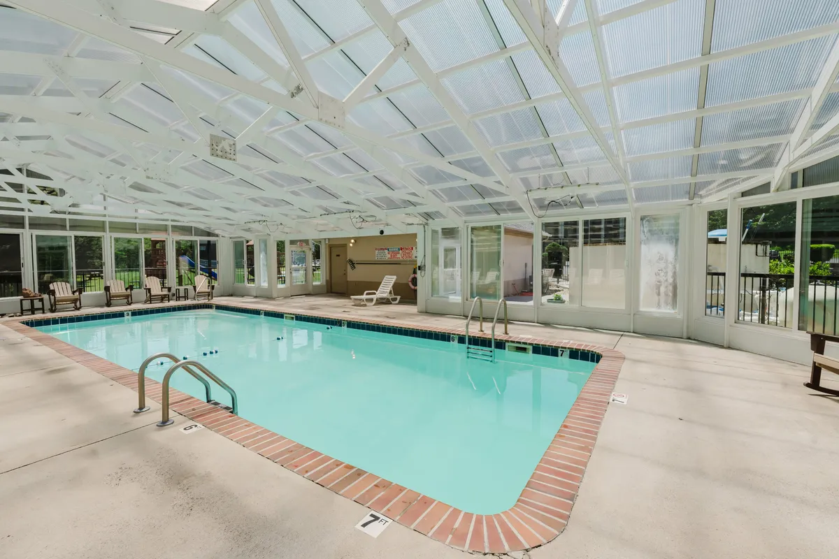 An inviting indoor swimming pool is surrounded by comfortable seating beneath a glass roof, creating a bright, cheerful space for swimming and relaxation regardless of the weather outside.