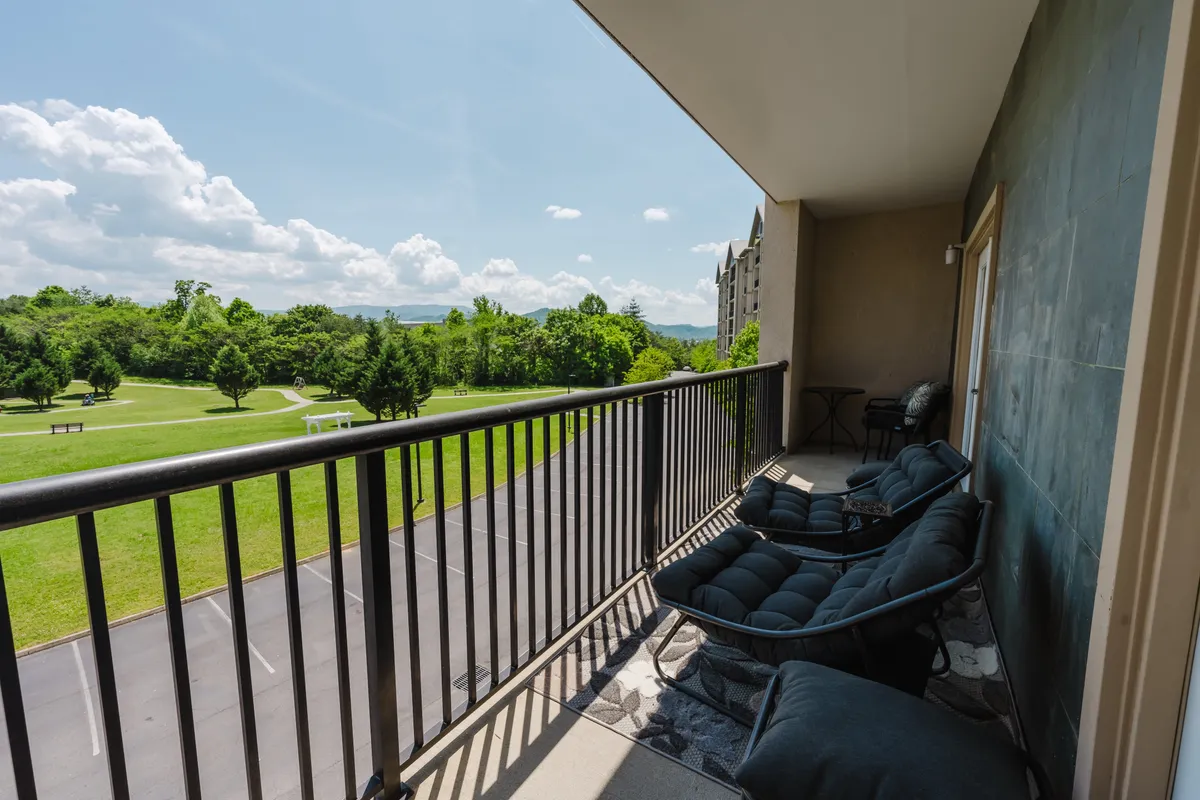A tranquil balcony scene featuring comfortable seating with sweeping green landscape views under a bright blue sky. The space invites guests to relax outdoors, socialize with friends, or wind down after exploring the lively local nightlife and attractions.