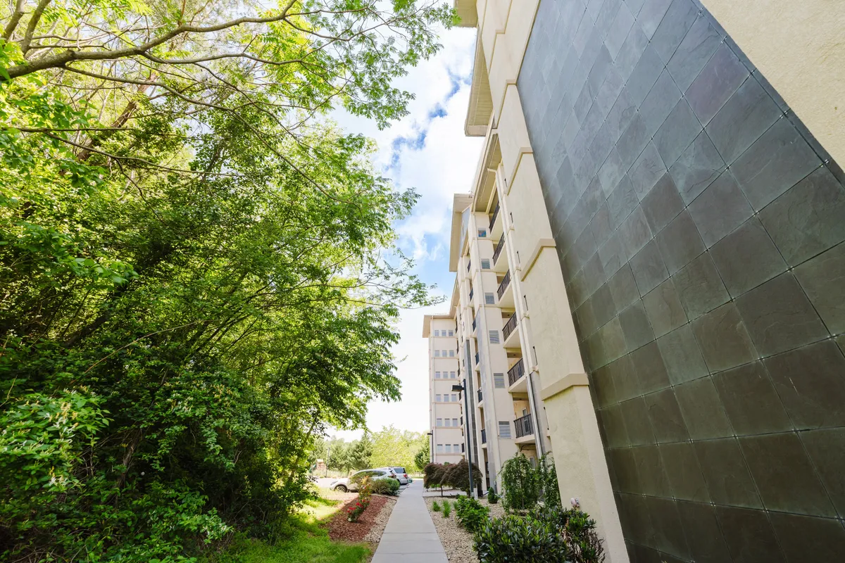 This image showcases the exterior of the resort building, surrounded by lush greenery and a peaceful pathway inviting guests to stroll and explore the natural setting. The scene evokes a sense of tranquility and connection with nature.
