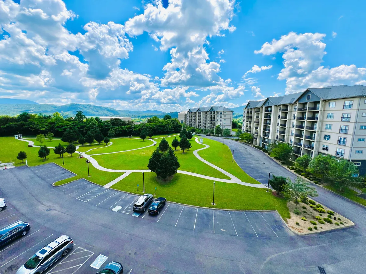 Expansive green lawns with walking paths meander in front of residential buildings, with a stunning mountain backdrop. The scene is bathed in soft natural light, inviting guests to explore or unwind while soaking in sweeping vistas.