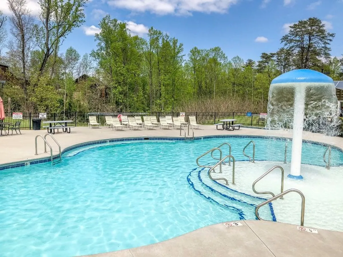 A sunlit outdoor pool area surrounded by lounge chairs and lush greenery. The inviting pool is perfect for swimming, basking in the sun, or hosting family gatherings, set against a backdrop of cheerful outdoor energy.