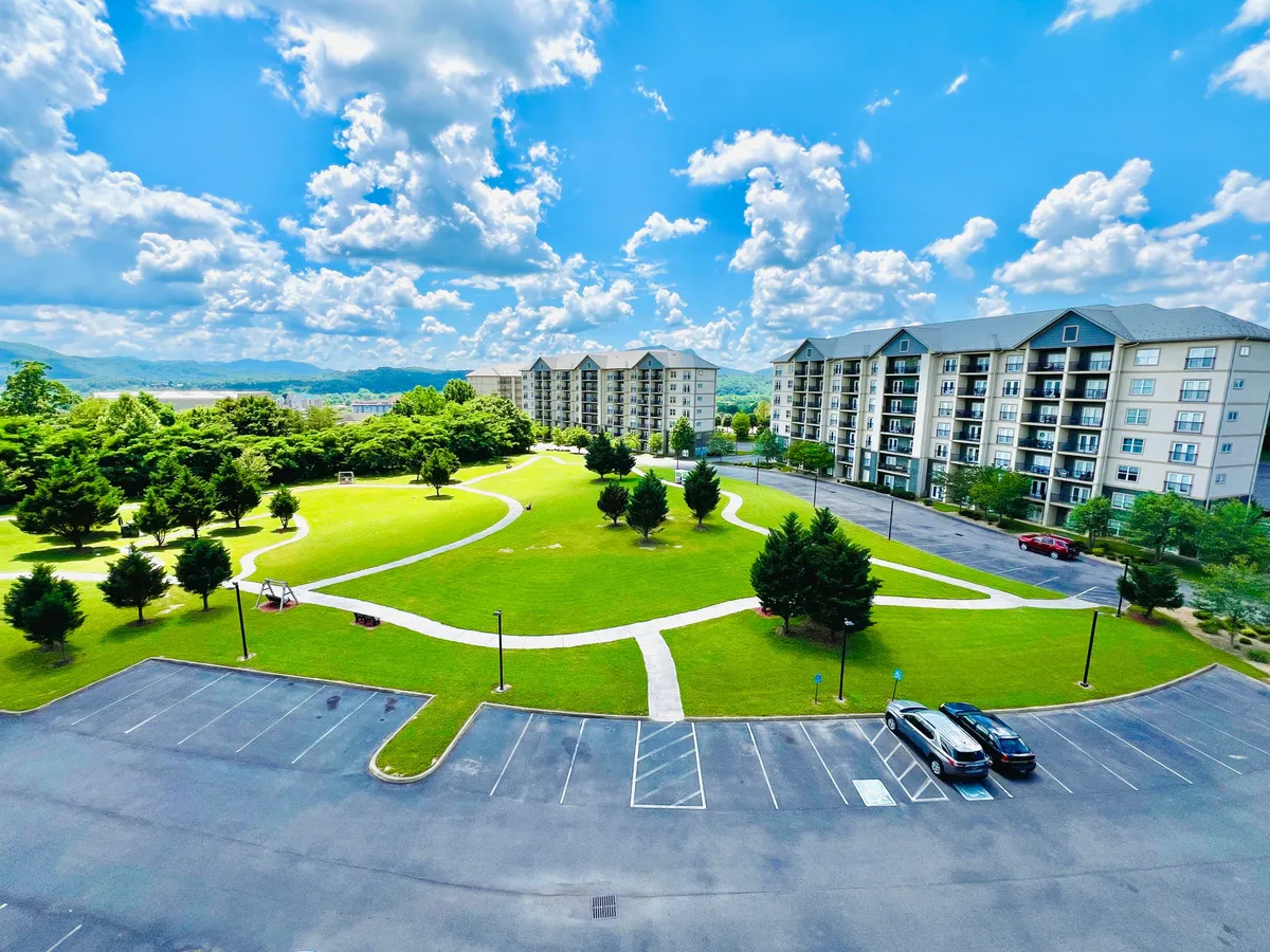 An inviting outdoor space with a bright green lawn, walking paths, residential buildings, and playground equipment. The scene is lively yet relaxed, inviting families and guests to walk, picnic, and play in the open air.